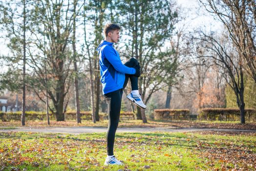 Young Male Runner Stretching in the Park in Cold Sunny Autumn Morning. Healthy Lifestyle and Sport Concept.