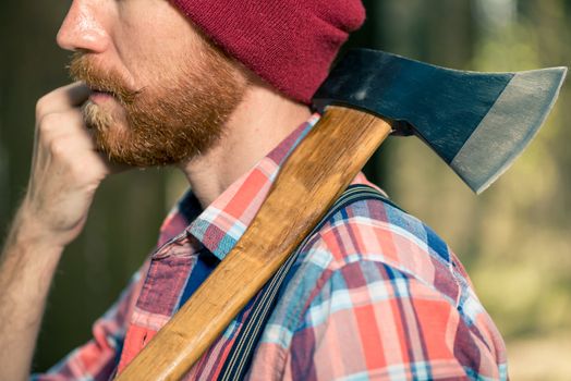 a forester with a red beard with an ax on his shoulder walks thr
