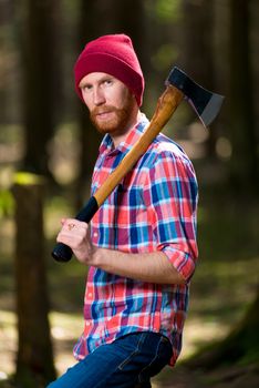 portrait of a serious hipster forester with an ax in the woods