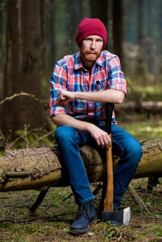 portrait of an experienced forester with an ax sitting on a fell
