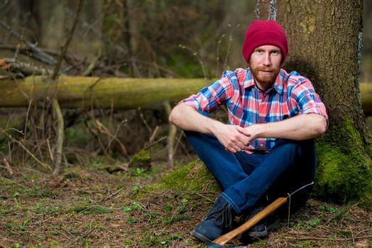 tired bearded forester with an ax on the relax in the forest