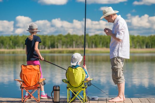 father teaches his children to fish on a fishing pole at the pie