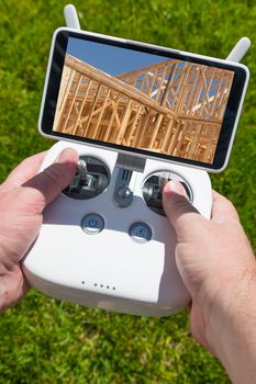 Hands Holding Drone Quadcopter Controller With Construction House Framing on Screen.