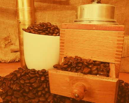 Vintage coffee mills, coffee beans and white cup filled coffee beans on wooden background