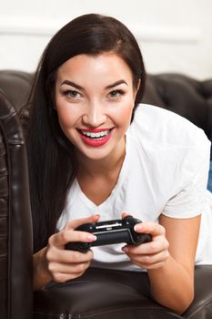 Woman gamer lies on brown leather sofa and plays a video game