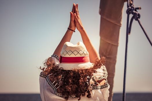Woman doing yoga exercises, rear view of a female standing in yoga asana on the sailboat among sea, cleansing of aura, meditating on vacation, happy healthy summer holidays
