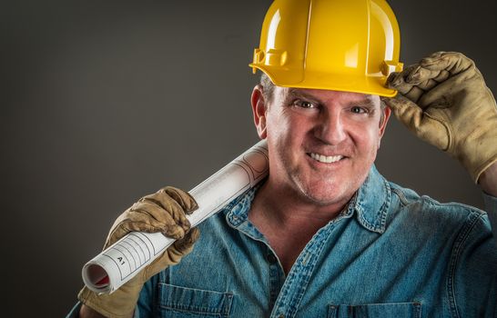 Smiling Contractor in Hard Hat Holding Floor Plans With Dramatic Lighting.