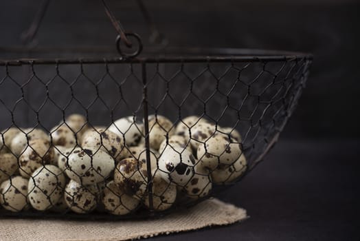 Wire mesh basket with quail eggs. Dark food photography. Rustic background, selective focus and diffused natural light. A different type of concept image for Easter. Copy space.