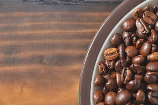 Edge of a saucer with coffee beans on a wooden board.