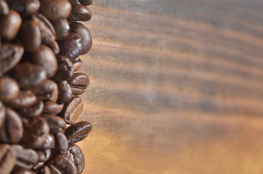 Many coffee beans lie on the left on a wooden background.