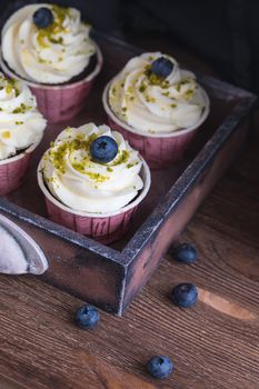 Homemade chocolate muffins or cupcakes with vanilla cream and pistachio on the wooden background