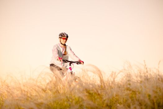 Young Woman Riding Mountain Bikes in the Beautiful Field of Feather Grass at Sunset. Adventure and Travel.