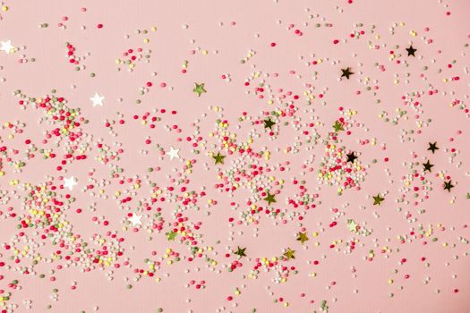 Golden star sprinkles and ice cream sprinkles on pink. Festive holiday background. Celebration concept. Top view, flat lay.