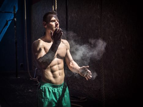Shirtless man using chalk or magnesium powder in gym