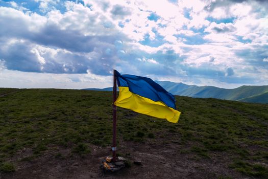 Ukrainian flag, set at the peak of the mountain against the background of a boundless blue sky with white clouds