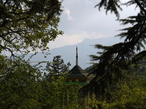 Arbor with a wooden roof and a sharp spire on it against the background of green trees and boundless mountains