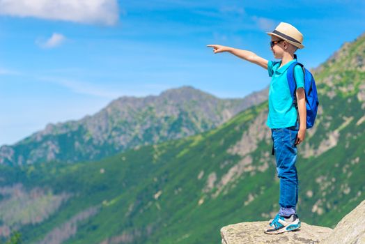 portrait of a boy traveler standing on a rock and pointing at a mountain