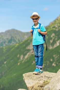 vertical portrait of a young traveler with a backpack high in the mountains on a rock
