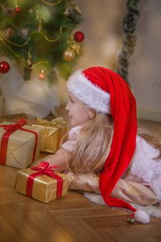 Girl in Santa hat dreaming under Christmas tree with gifts