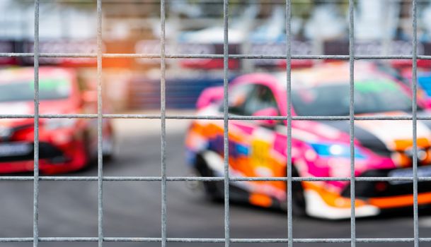 Motorsport car racing on asphalt road. View from the fence mesh netting on blurred car on racetrack background. Super racing car on street circuit. Automotive industry concept.