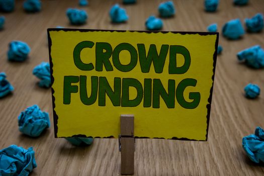 Text sign showing Crowd Funding. Conceptual photo Fundraising Kickstarter Startup Pledge Platform Donations Clothespin holding yellow paper note crumpled papers several tries mistakes.