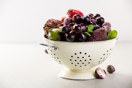 Purple fruits and vegetables in colander - space for text