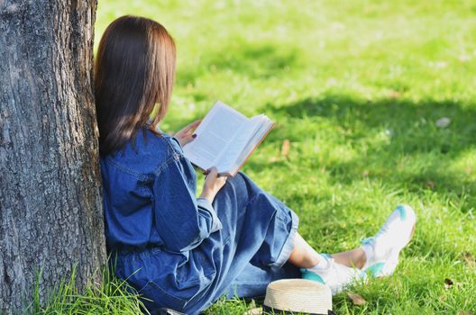 Beautiful, happy young girl student reading a book sitting on green gras