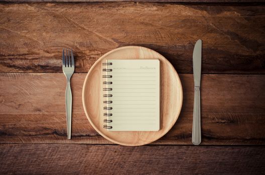 Notebook in the wooden plate with a spoon and a knife laying beside a table,Concept for perception