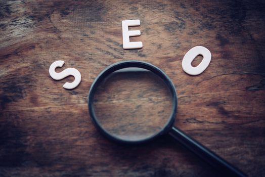 The words "S E O" and the magnifying glass on the wooden floor - Search Engine Optimization Concept