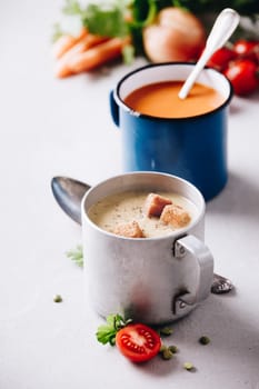 Pea and tomato soups and ingredients on concrete background