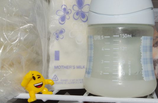 lot of frozzen breast milk in storage bags stored in the freezer and baby bottle with fresh expresed breastmilk
