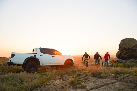 Friends Riding Bikes in the Mountains in front of the Pickup Off Road Truck at Sunset. Adventure and Travel Concept