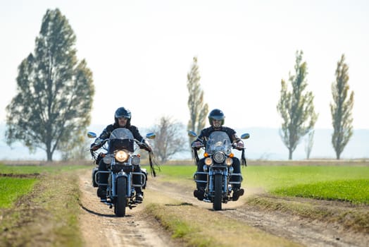 Two Motorcycle Drivers Riding Custom Chopper Bikes on an Autumn Dirt Road in the Green Field. Adventure Concept.