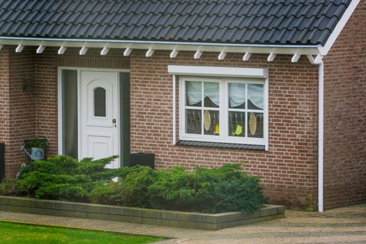 front exterior of a luxurious dutch bungalow with a garden, front door with decorated window, home in a small village of the Netherlands