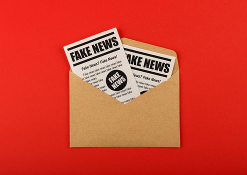 Envelope with FAKE NEWS newspapers over red