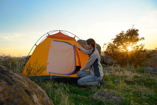Young Woman Assembling the Tent at Sunset in the Mountains. Adventure and Travel.