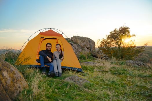 Young Couple Sitting near Tent at Beautirul Evening in the Mountains. Adventure and Family Travel.