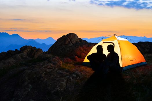 Young Couple Sitting near Illuminated Tent and Looking at Each Other at Beautirul Evening in the Mountains