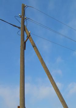 Old wooden support of power transmission lines 0.4 kV with wires and insulators on a blue sky background, vertical image