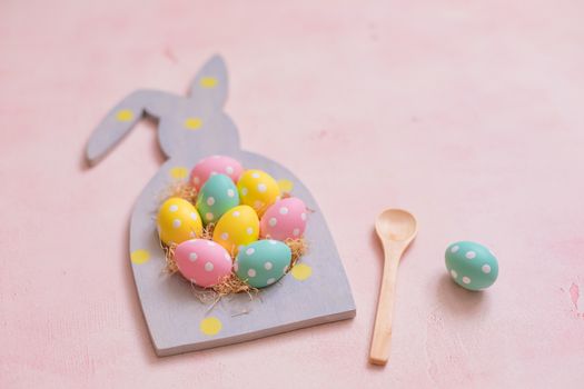 Colorful polka dot easter eggs in rabbit-shaped frame on pink concrete background