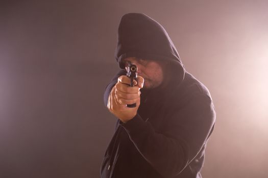Man in black hoodie points handgun in smoke