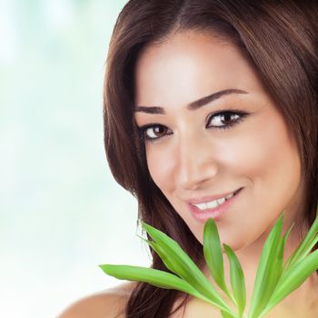 Closeup portrait of beautiful brunet woman with fresh green leaves over blue blur background, healthy lifestyle, enjoying day spa

