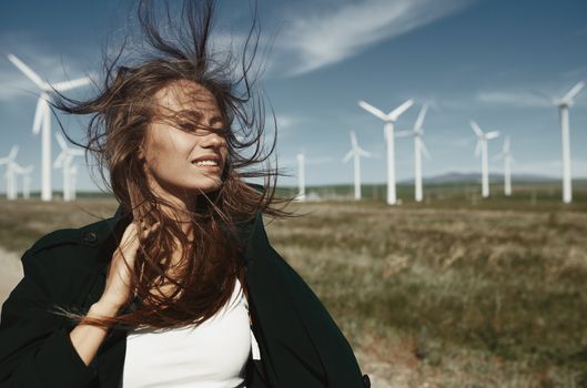 Woman with long tousled hair next to the wind turbine with the w