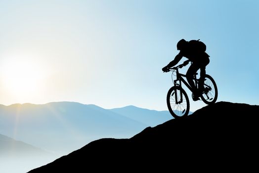 Silhouette of Cyclist Riding the Bike Down the Rock at Sunrise. Extreme Sport and Enduro Biking Concept.