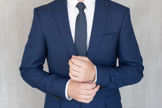 Torso of anonymous businessman wearing beautiful fashionable classic navy blue suit against grey backgound.