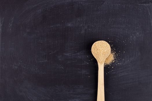 Brown cane sugar in wooden spoon on black background. 