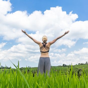 Relaxed healthy sporty woman, arms rised to the sky, enjoying pure nature at beautiful green rice fields on Bali.