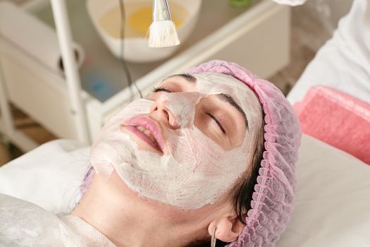 Young woman in beauty salon does make application of moisturizing, softening, regenerating mask.