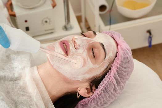 Young woman in beauty salon does rejuvenating, toning procedure darsonval on the face.