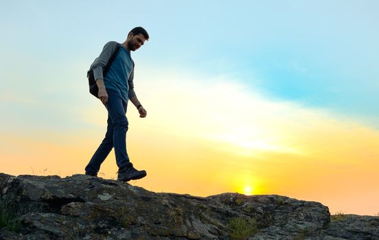 Young Happy Man Traveler Hiking with Backpack on the Rocky Trail at Warm Summer Sunset. Travel and Adventure Concept.